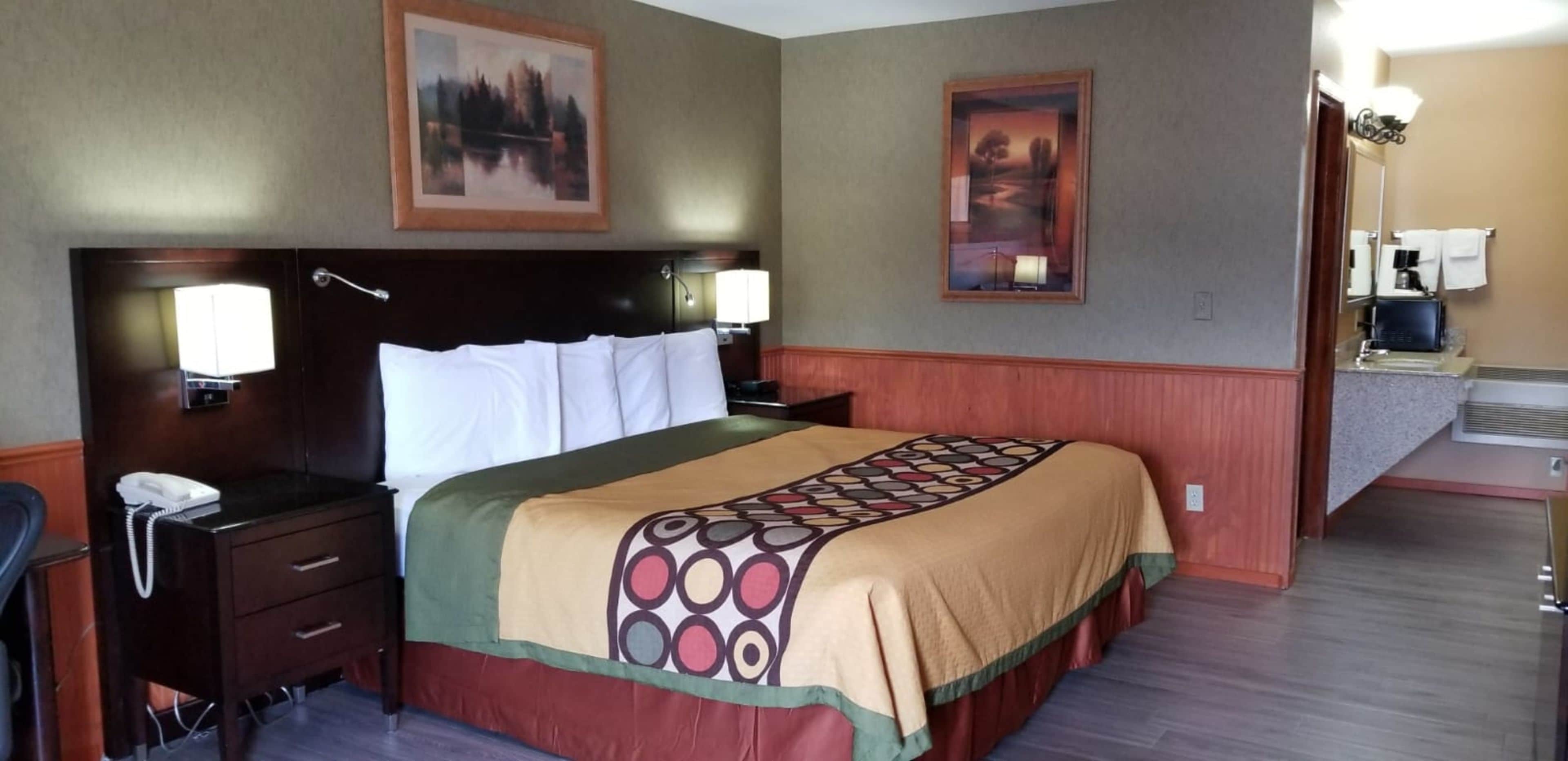 A hotel room with a large bed, a desk with a phone, two wall-mounted lamps, and two framed pictures on the walls.