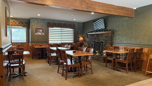 Un restaurante con mesas y sillas de madera, una chimenea de piedra y vistas al exterior a través de amplios ventanales.