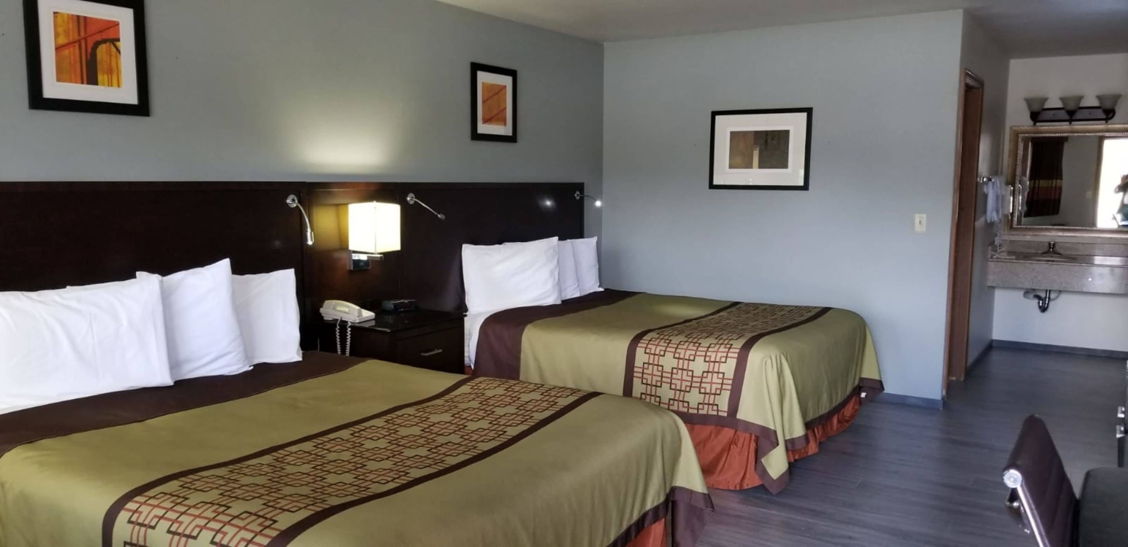 Une chambre d’hôtel avec deux lits, une table de chevet avec une lampe, un téléphone et un miroir au-dessus du lavabo.
