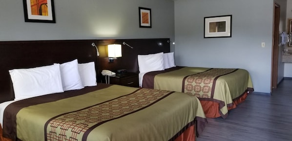 Habitación de hotel con dos camas, cada una con una colcha estampada y almohadas blancas. Hay una mesita de noche con una lámpara y un teléfono.