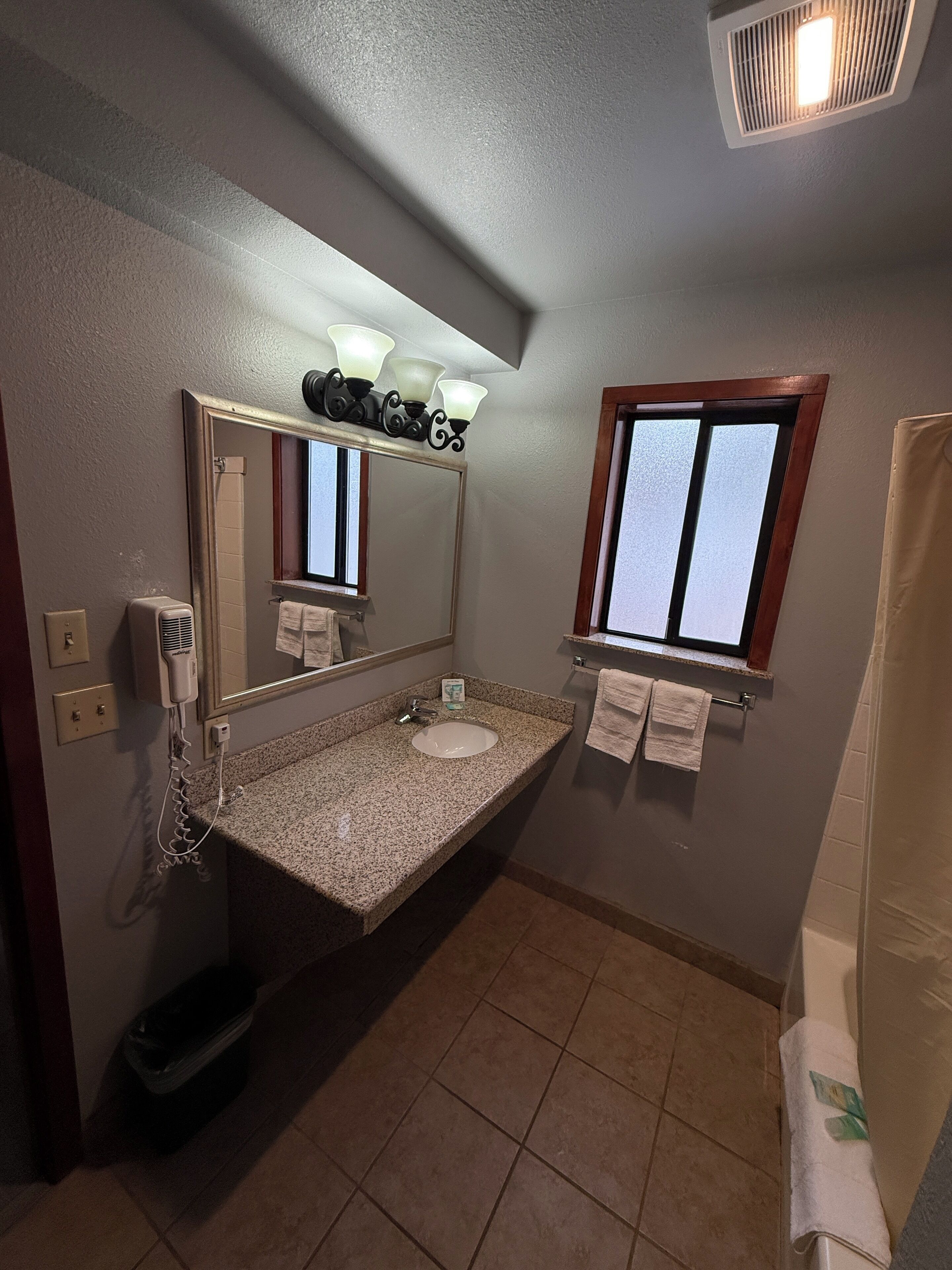 Baño con lavamanos de granito, espejo con luces arriba, ventana y cortina de ducha.