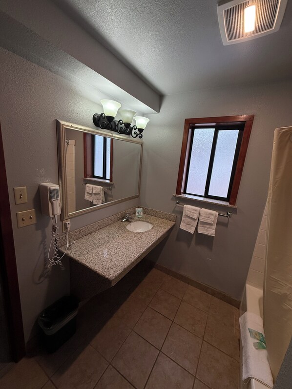 A bathroom with a granite countertop sink, a mirror with lights above, a window, and a shower curtain. - Stewart Lodge (Cle Elum)