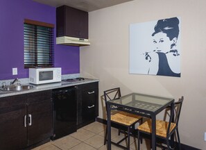 A compact kitchen with a microwave, stove, and dark cabinets. A glass table with wicker chairs is positioned near the window.