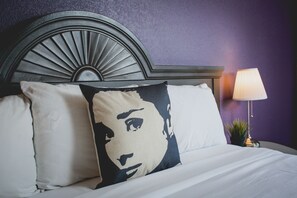 A bed with white linens, a headboard with a fan design, and a lamp on a side table.