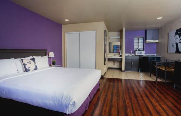 A hotel room with a large bed, a desk, and a kitchenette.
