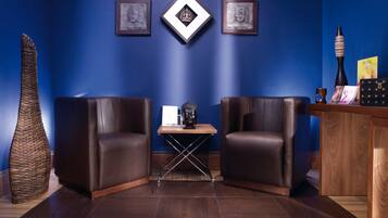 A room with two leather chairs, a small table with a Buddha statue, framed artwork on the wall, and a wooden desk with a vase and a book.