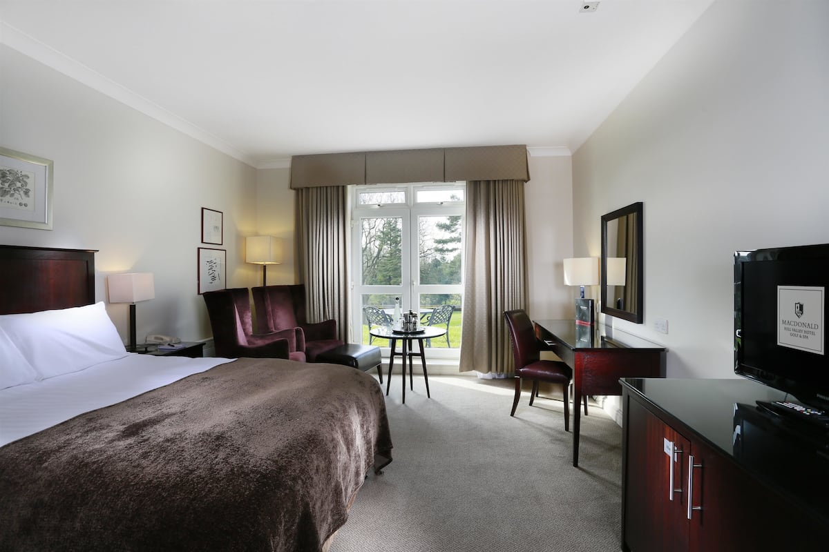 A hotel room with a bed, a desk, a chair, a television, and a window with curtains.