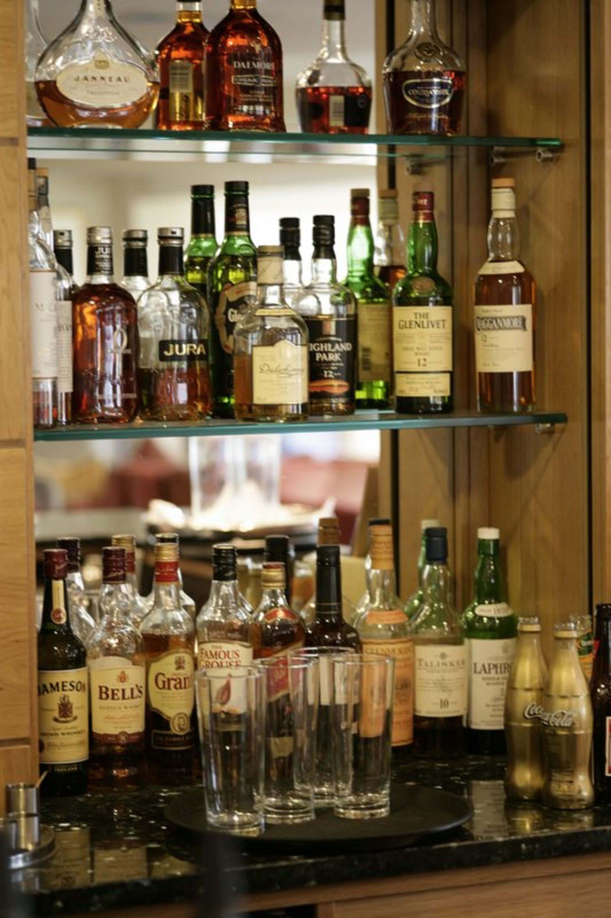 Zona de bar con varias estanterías llenas de botellas de licores y vasos.