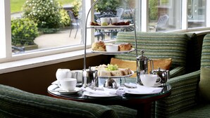 Una bandeja de tres niveles para servicio de té sobre una mesa junto a una ventana con vistas a un jardín.