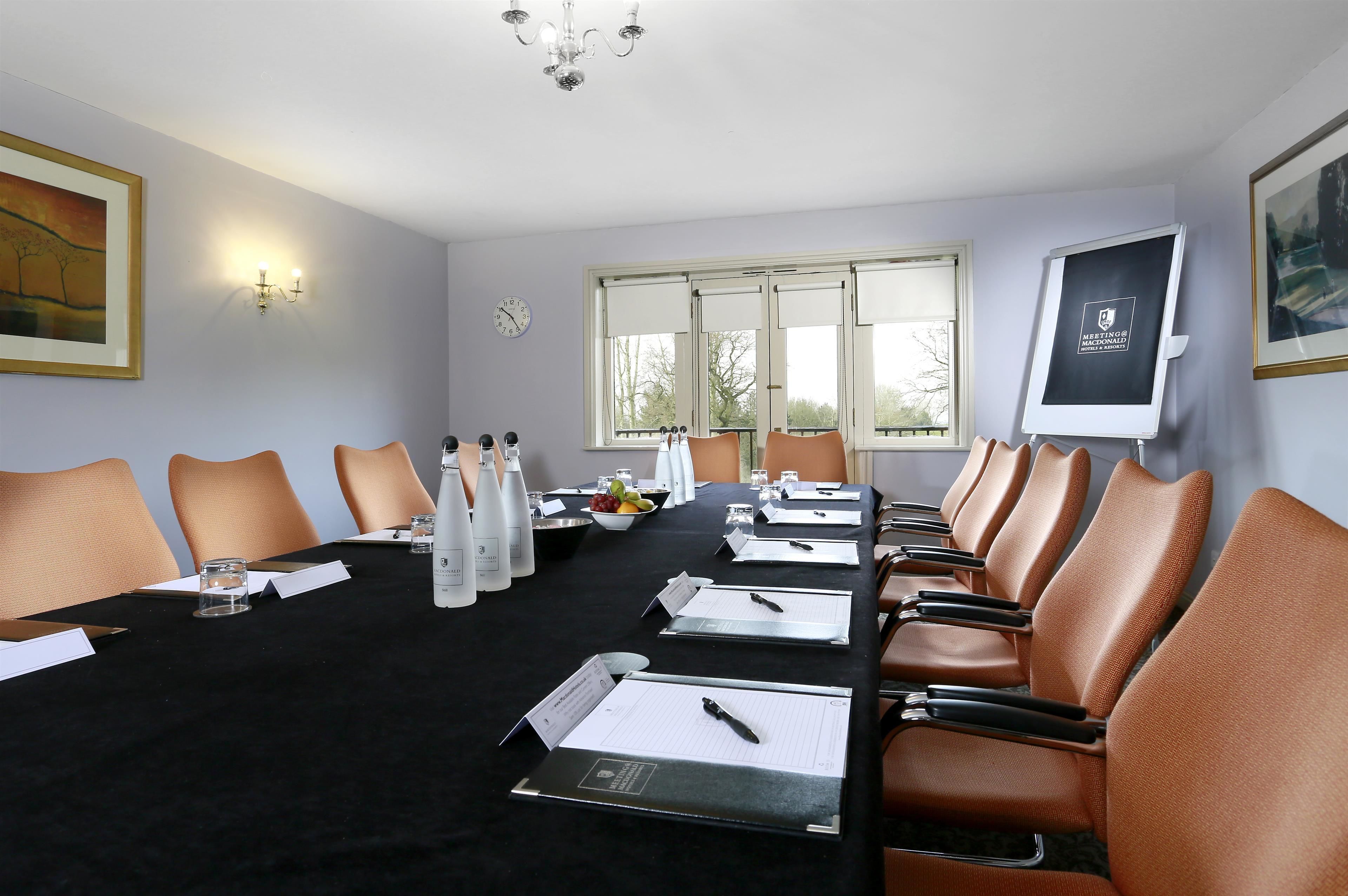 A conference room with a long table, chairs, nameplates, water bottles, and a clock on the wall.