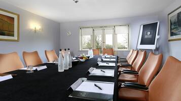 A conference room with a long table, chairs, nameplates, water bottles, and a clock on the wall.