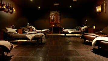 Relax in a serene spa room with a central seating area, reclining chairs, and a cozy fireplace.