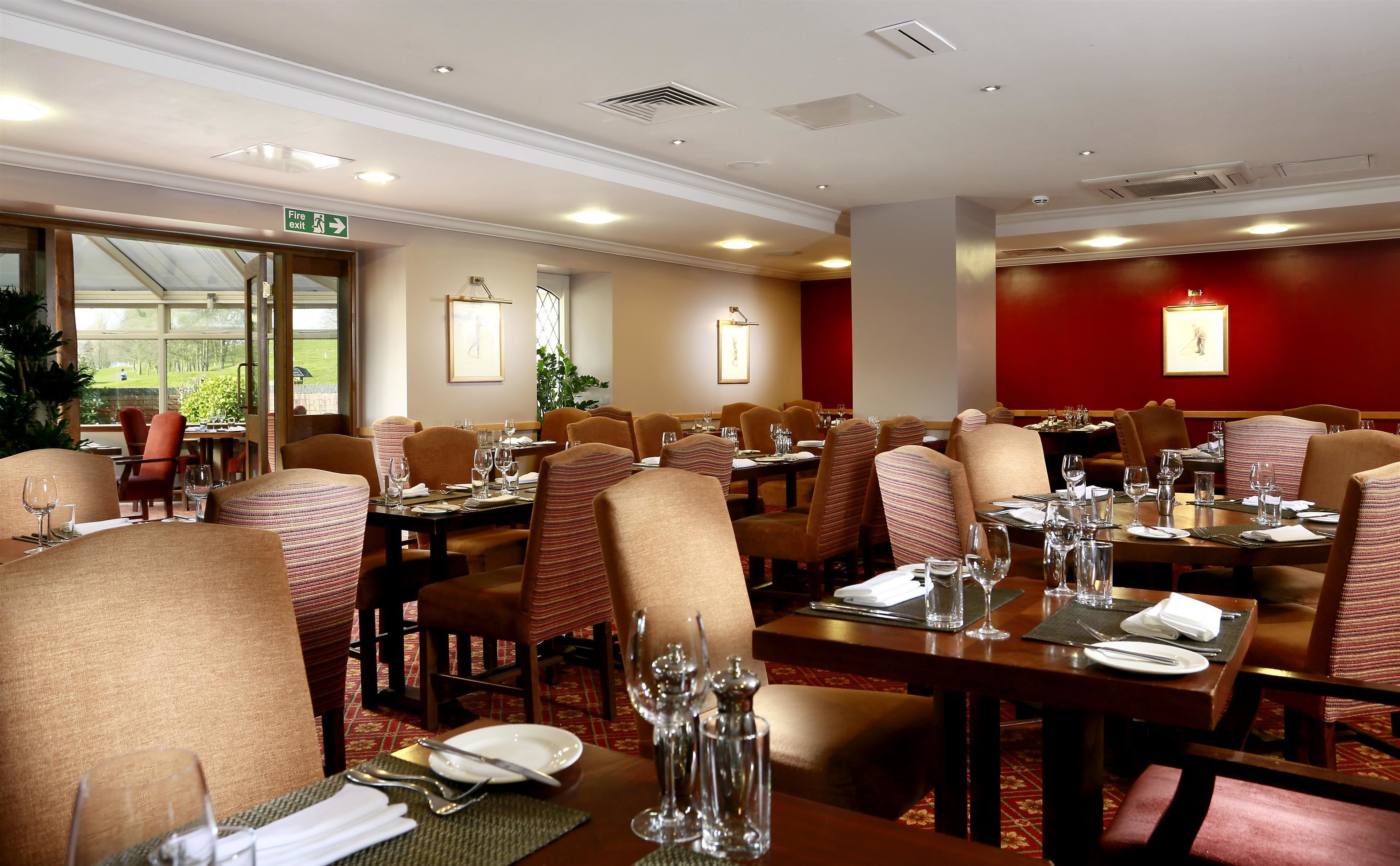 A well-lit dining area with multiple tables and chairs, a fire exit sign, and framed artwork on the walls.