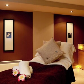 A hotel room with a bed, pillows, a blanket, and a nightstand with a lamp.