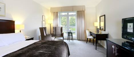 A hotel room with a large bed, a desk with a chair, a television, and a balcony with curtains.