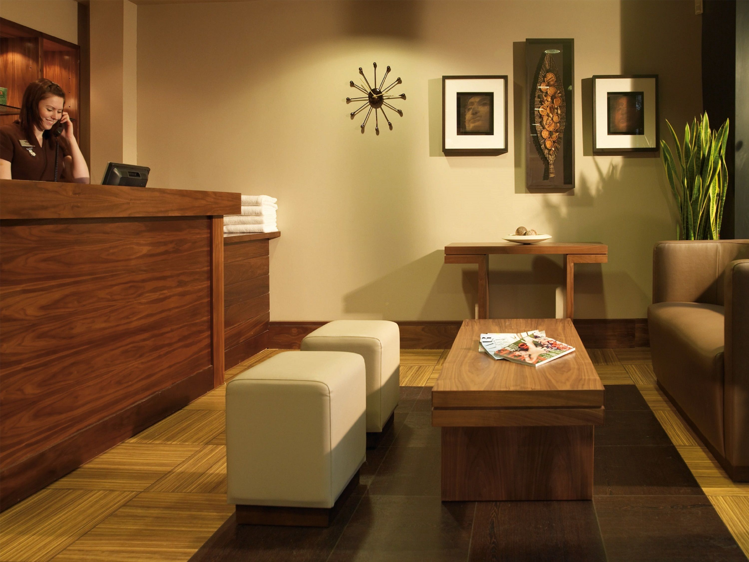 A reception area with a wooden reception desk, a white cushioned bench, a wooden table with magazines, and framed artwork on the wall.