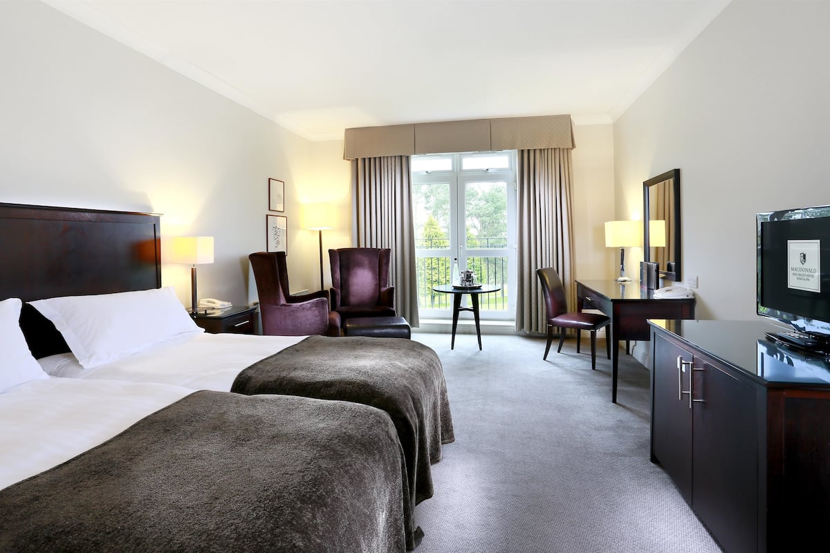 A hotel room with two beds, a desk, a chair, a television, and a window with curtains.
