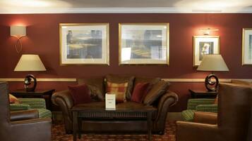 Une chambre d’hôtel avec un canapé en cuir marron, deux fauteuils, une petite table et des tableaux encadrés accrochés au mur.