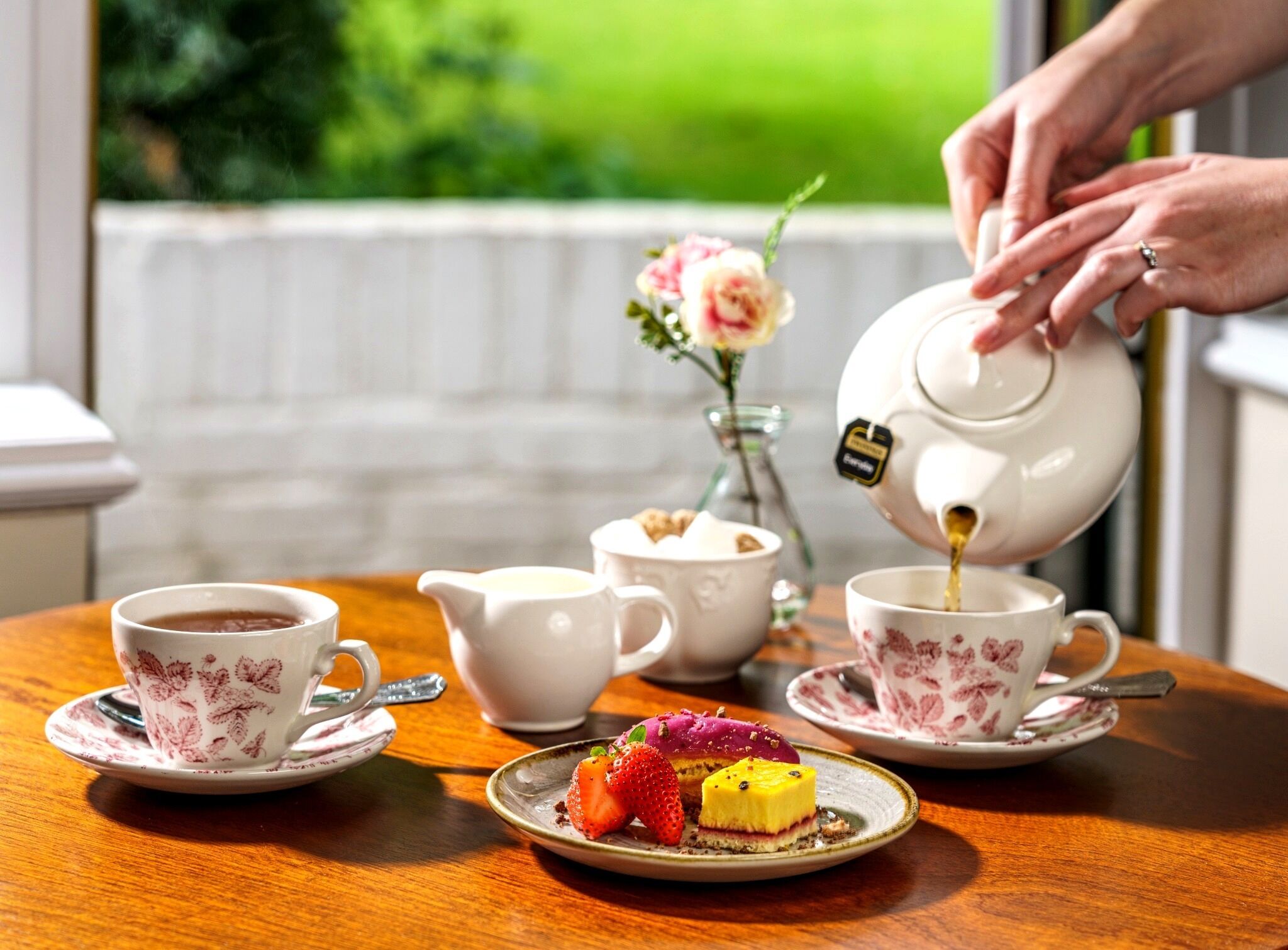 A table with a teapot, cups, a jug, and a plate with a dessert.
