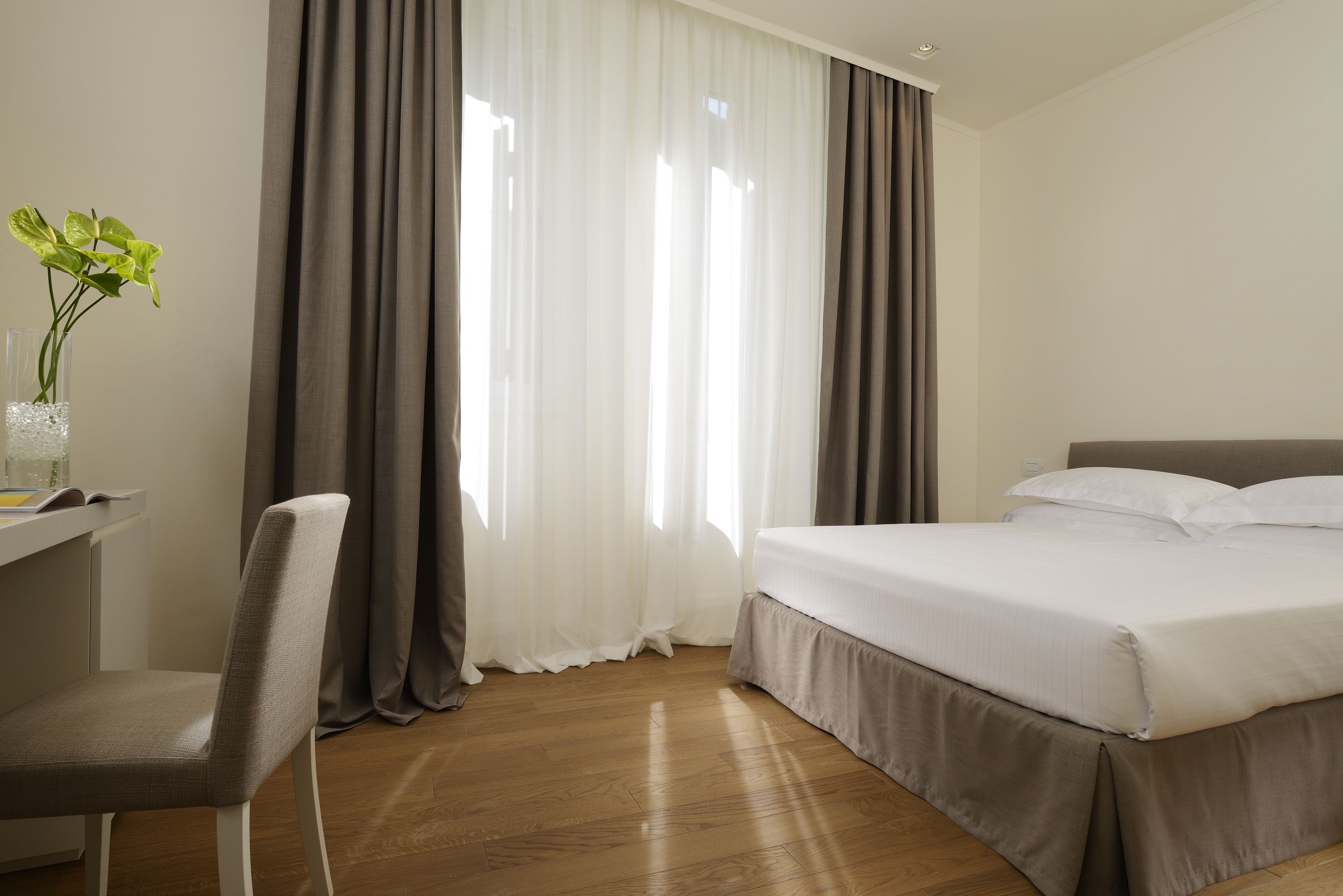 Una habitación de hotel con cama, escritorio, silla y ventana con cortinas.