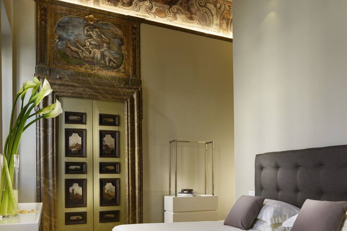 Une chambre à coucher avec un grand lit, un plancher en bois, un plafond décoratif et une porte ornée d’œuvres d’art.