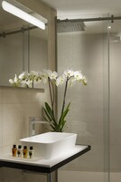 Un baño moderno con lavamanos blanco, un espejo y una zona de ducha.