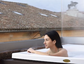 A person relaxing in a Jacuzzi with a view of a tiled roof and a statue in the background.