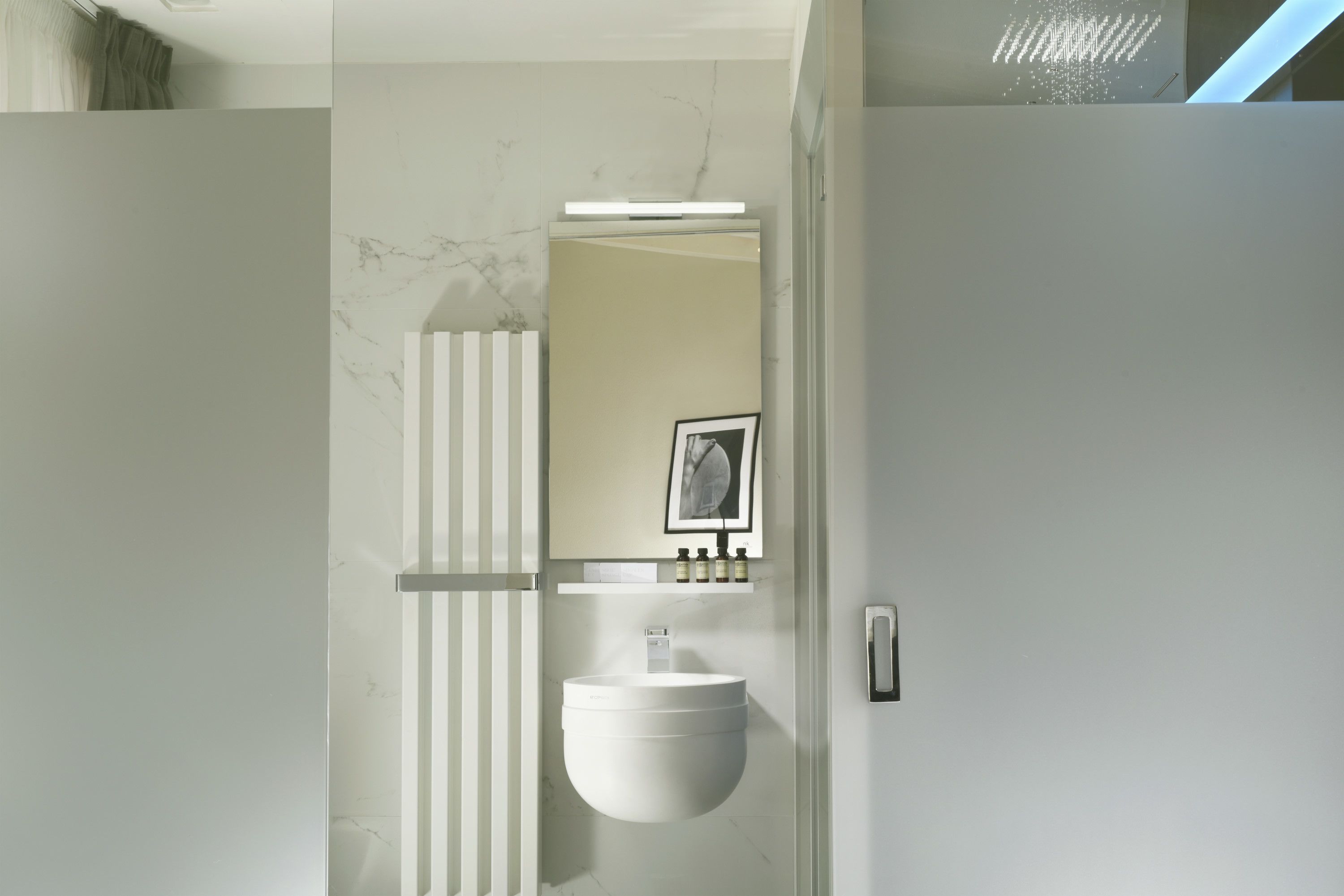 Een moderne badkamer met een witte wastafel, een marmeren spatwand en een spiegel aan de muur.
