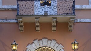 A building facade with a stone archway, a balcony with a flag, and two wall-mounted lights. - Locanda della Posta - Etruria Collection (Perugia)