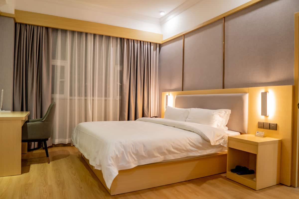Habitación de hotel con una cama grande, un escritorio, una silla y una mesita de noche con lámpara.