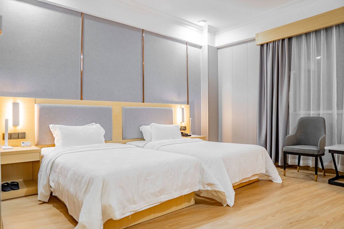 Habitación de hotel con dos camas, un escritorio, una silla y un ventanal con cortinas.