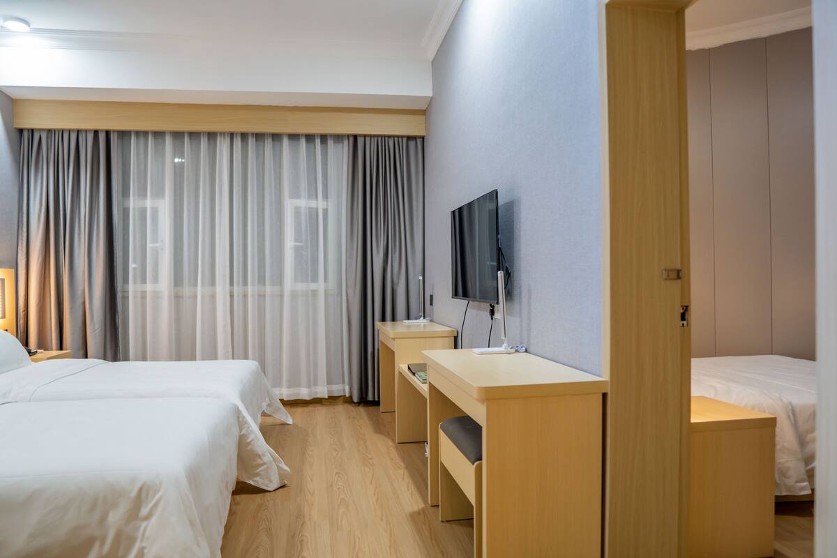 Habitación de hotel con dos camas, un escritorio, un televisor y un ventanal con cortinas.
