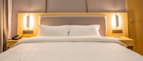 A hotel room with a large bed, two bedside tables with lamps, a telephone, and a wooden door.