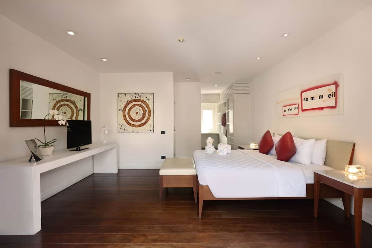 A modern hotel room with a bed, bedside table, TV, artwork, and a mirror.