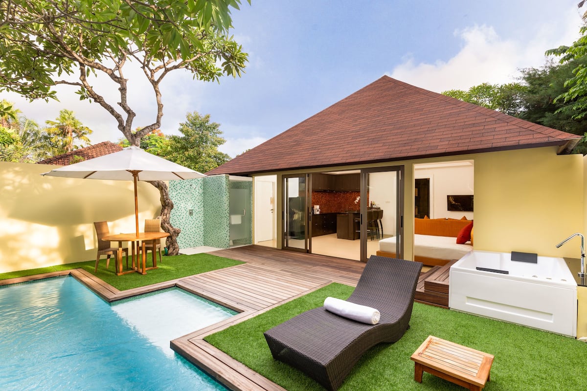 A modern outdoor pool area with a lounge chair, a small wooden table, and a white outdoor seating area.