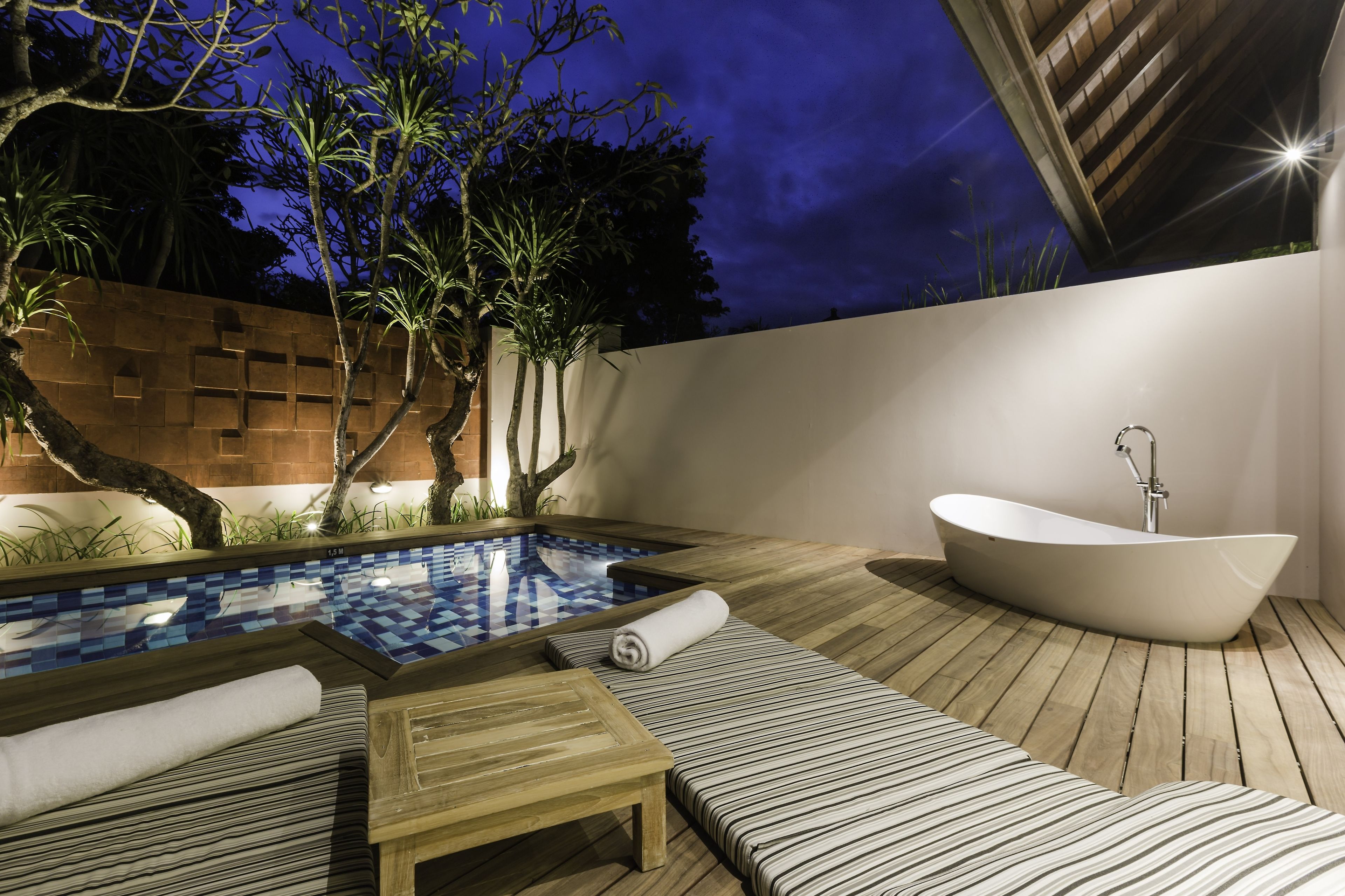 A modern outdoor pool area with a wooden deck, lounge chairs, a hot tub, and a small table.