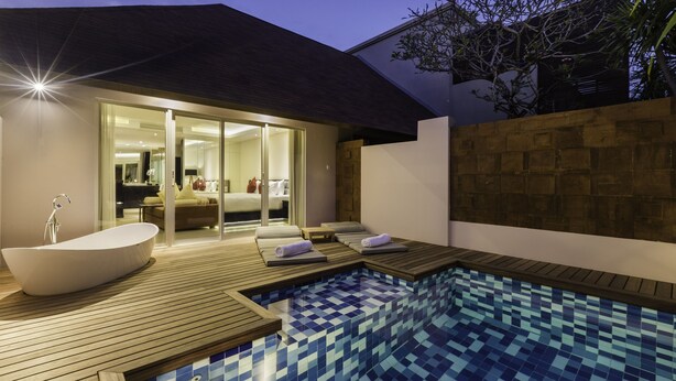 Un área de piscina moderna al aire libre con un jacuzzi, terraza de madera y un spa con paredes de vidrio.