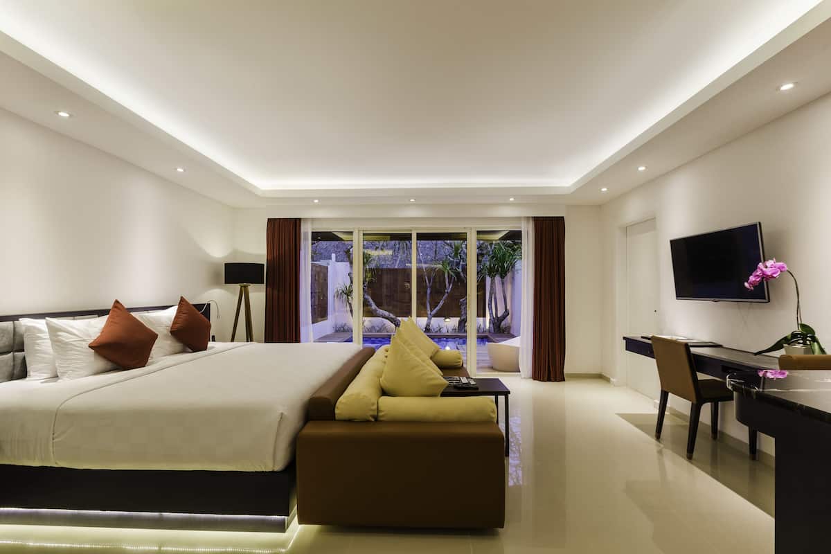 A modern hotel room with a large bed, a sofa, a desk, and a TV.