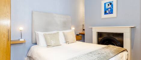 Quarto com cama, mesas de cabeceira, um quadro na parede e lareira.