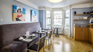 A modern dining area with a sofa, tables, chairs, and artwork on the walls. - Brightonwave (Brighton)