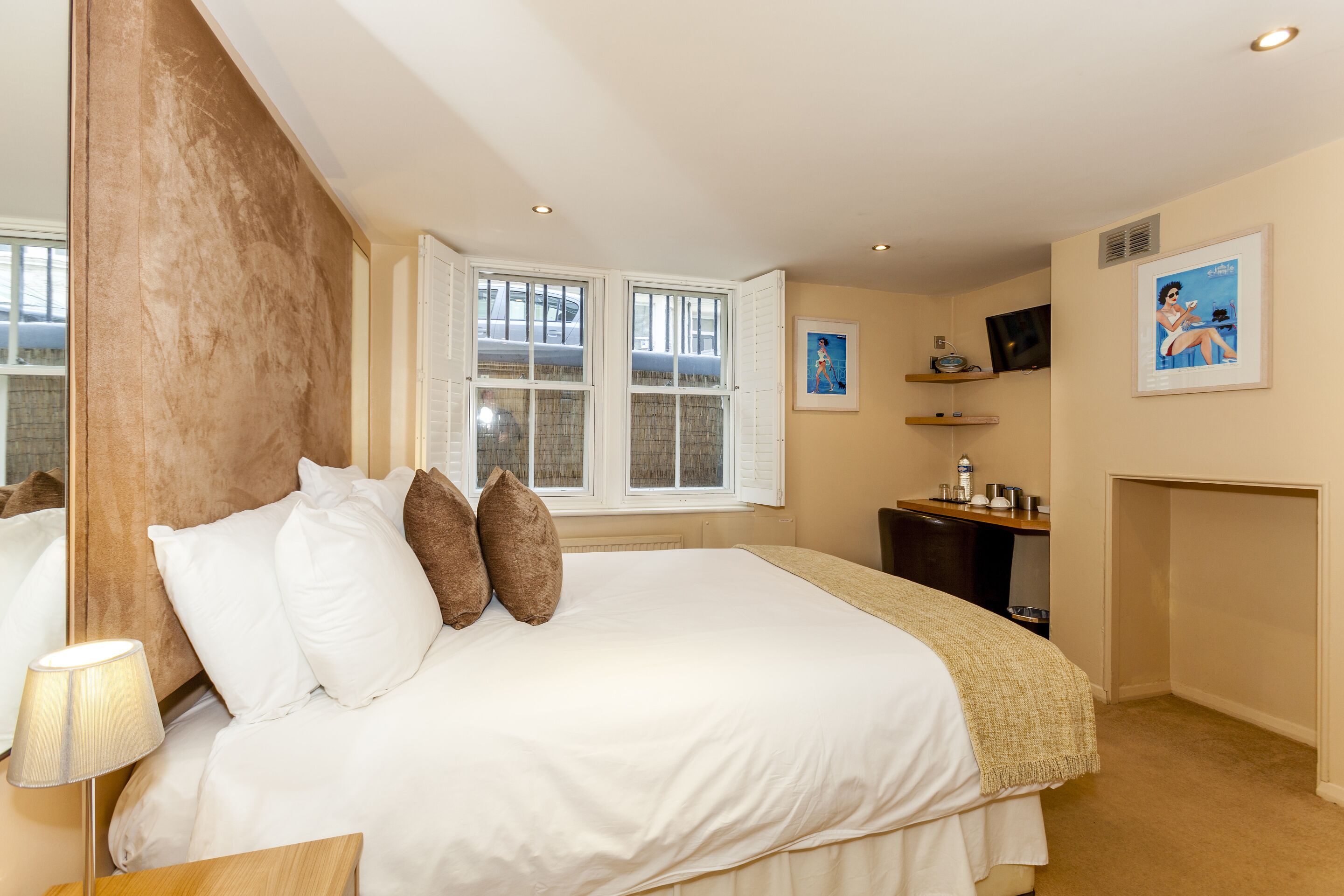 A neatly arranged bedroom with a large bed, a bedside table, a lamp, a television, and a framed picture on the wall.