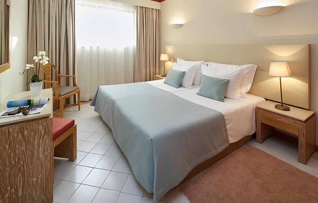 Habitación de hotel con cama, mesitas de noche, un escritorio, una silla y una ventana con cortinas.