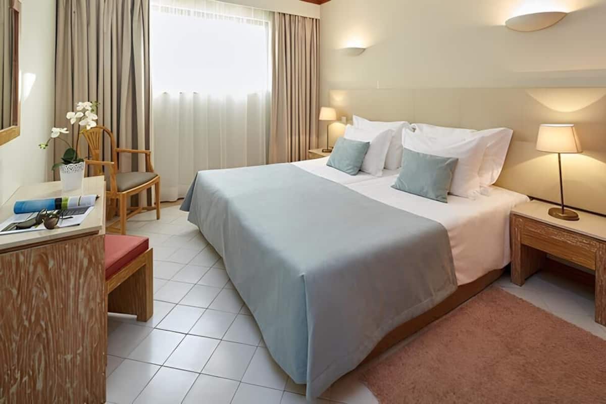 Habitación de hotel con cama, mesitas de noche, un escritorio, una silla y una ventana con cortinas.