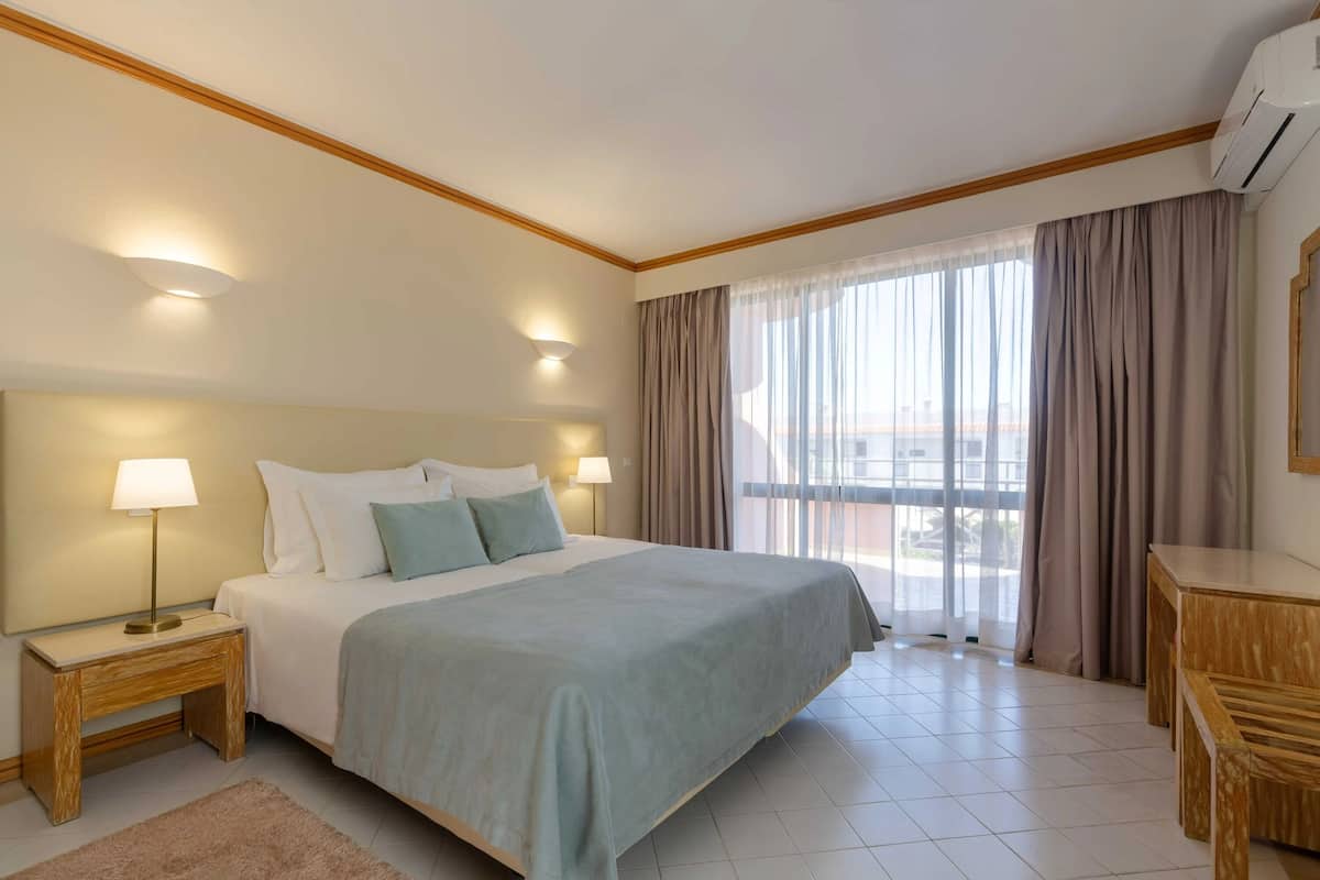A hotel room with a bed, bedside lamps, a desk, and a view through the window.