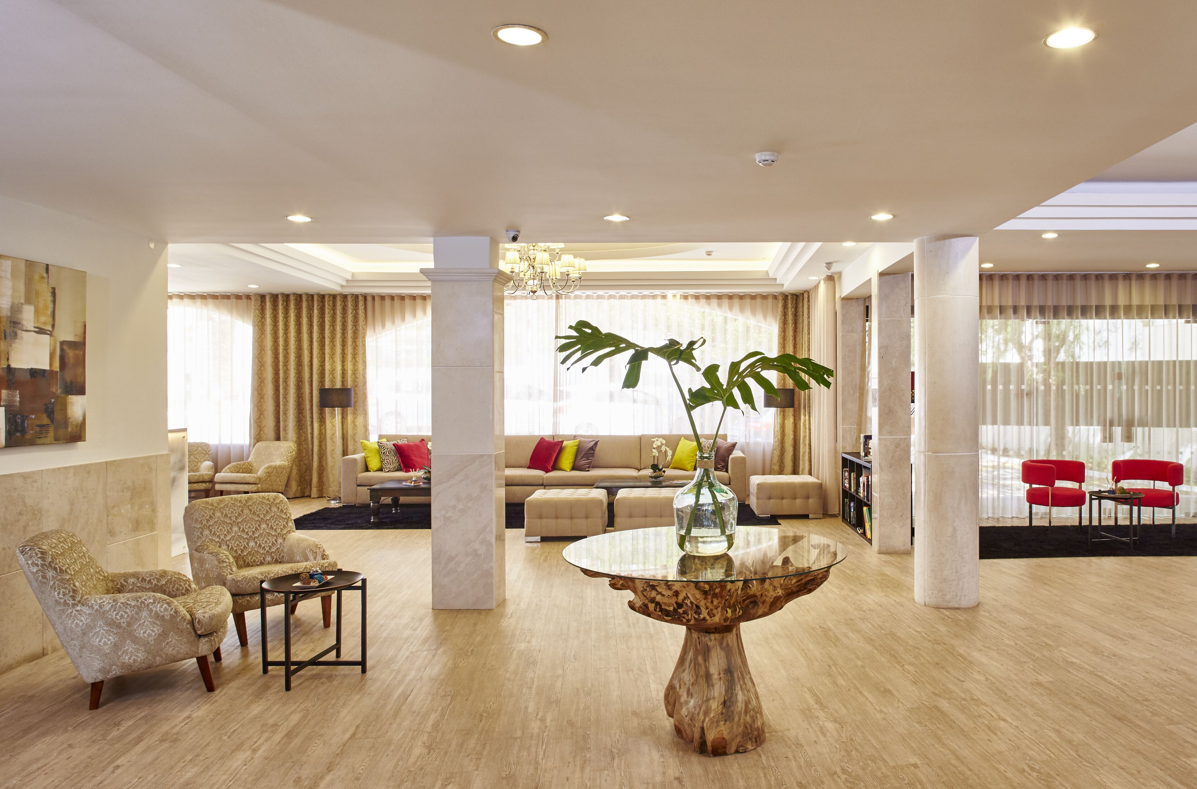 Un salón amplio con una mesa de centro redonda de vidrio, sofás color beige y sillas rojas.