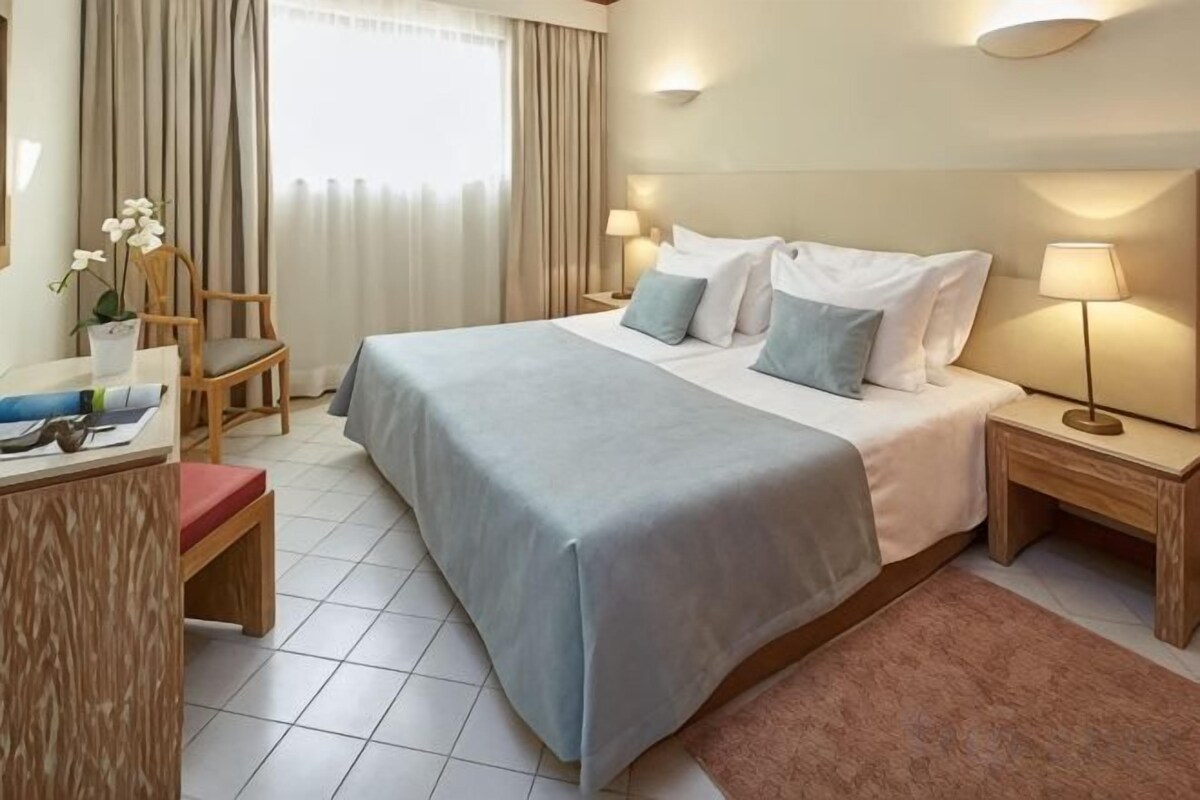 A hotel room with a bed, bedside tables, a desk, and a chair.