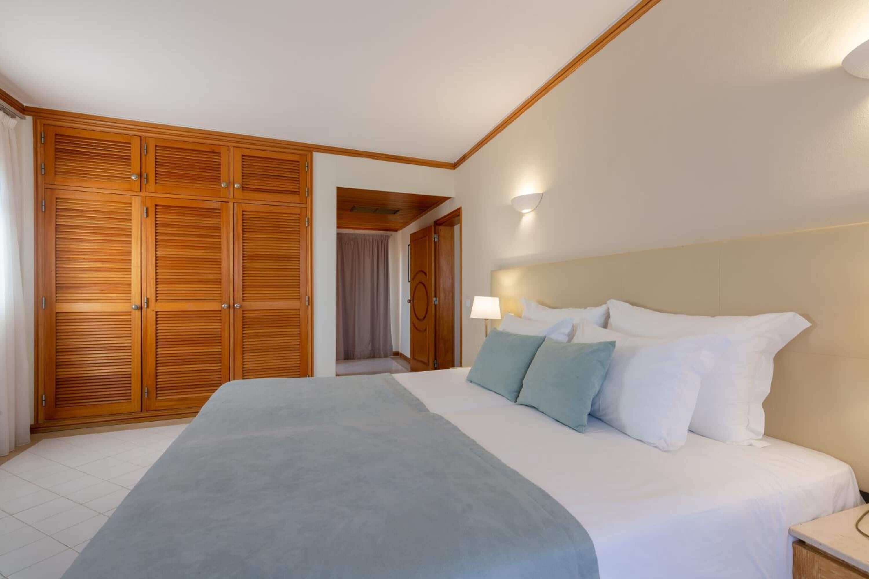 A hotel room with a large bed, wooden wardrobe, and a nightstand with a lamp.