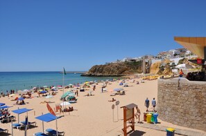 Een strand met ligbedden en parasols, een bewakingstoren en een stenen muur.