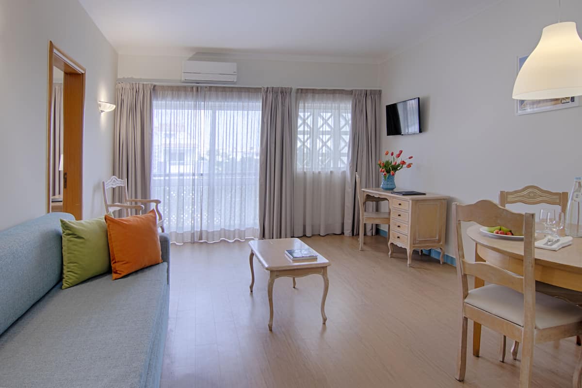 A well-lit room with a sofa, a dining table, a TV, and a window with curtains.