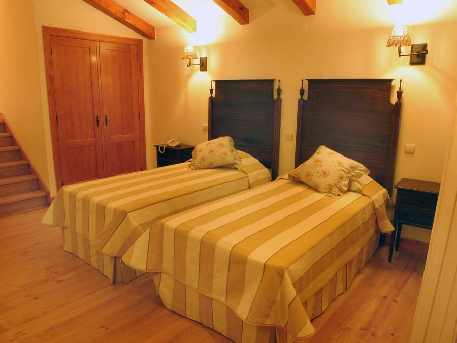 A room with two beds, wooden flooring, a staircase, and a wooden wardrobe.